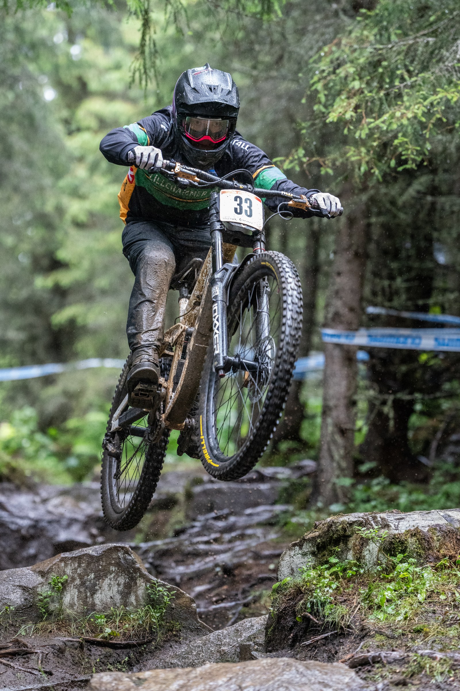 Terrengsyklist med startnummer 33 over steiner på en smal sti i granskogen.